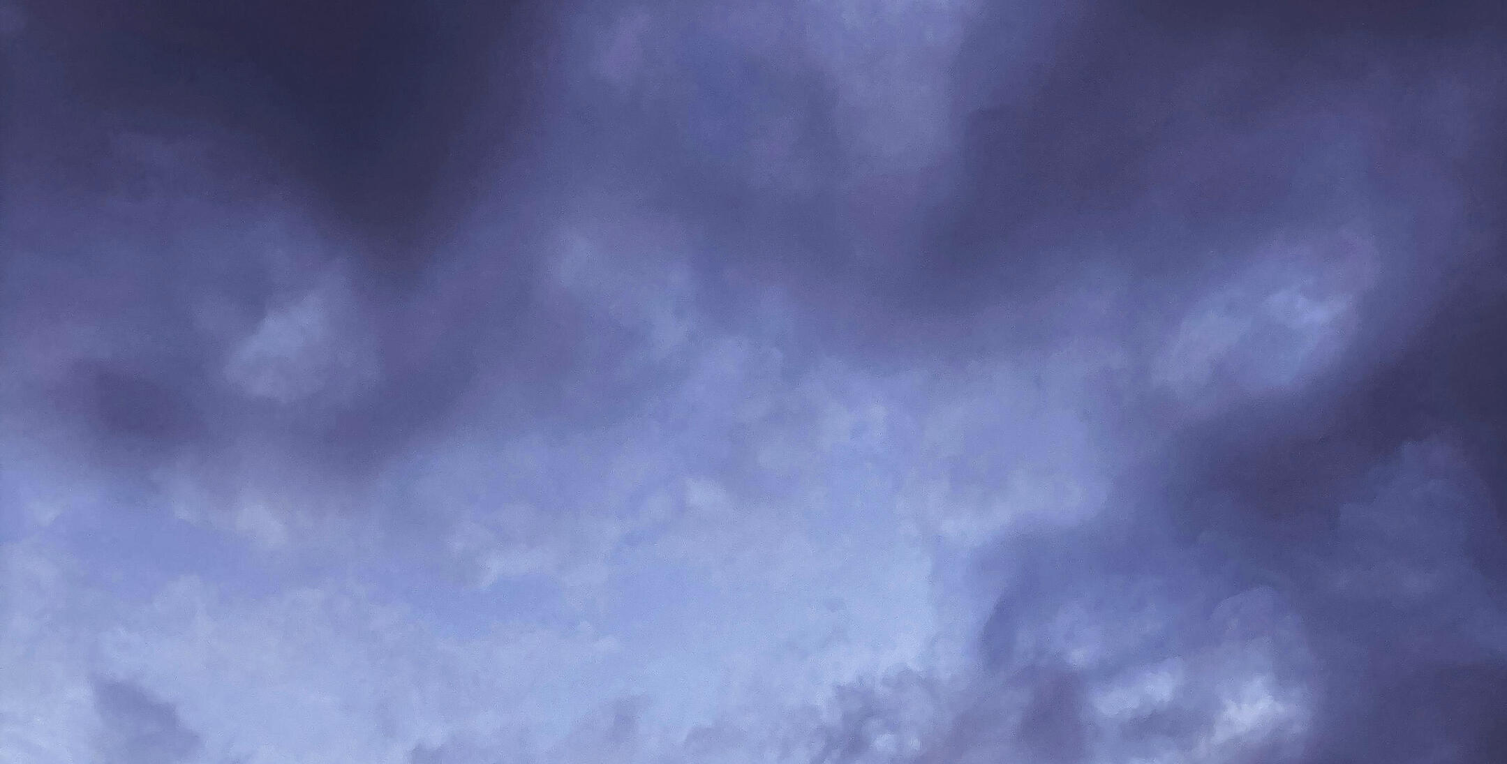 A photo of dusky purple clouds against a pale blue sky